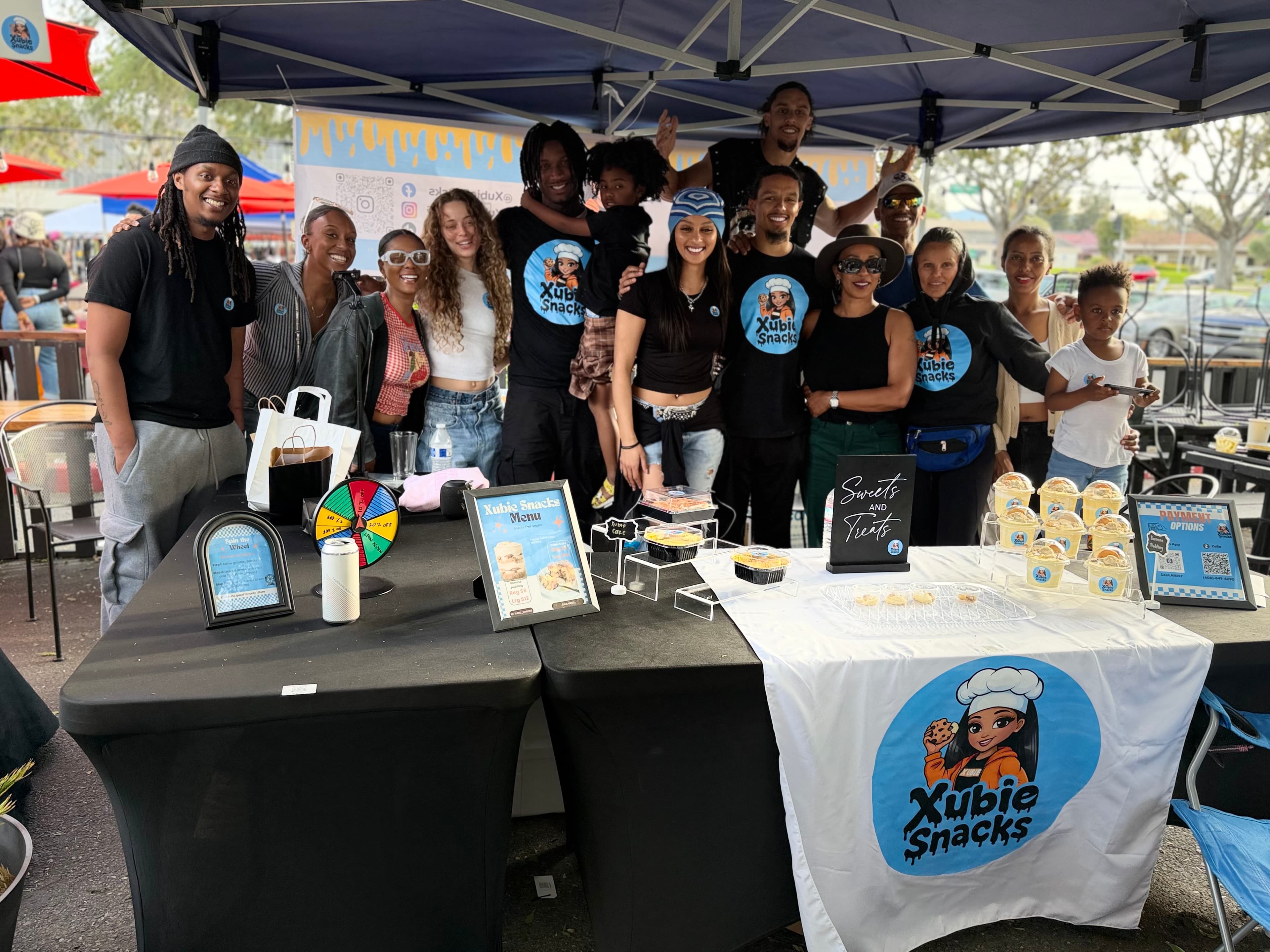 Xubie Snacks booth with community gathered around desserts and branded table